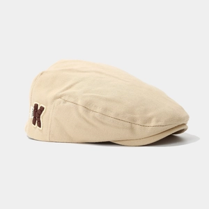 Close-up of beige cotton beret showing twill texture and brown letter K patch detail