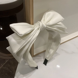Close-up of white satin triple bow headband with high crown design and silk texture