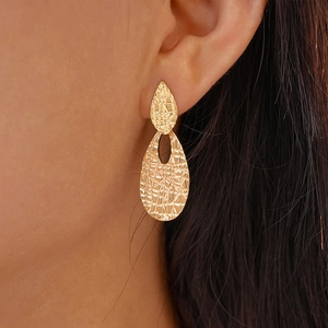 Close-up of golden teardrop geometric earrings with textured finish worn by a model