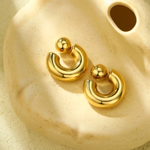 Detail of gold polished C-shaped stainless steel hoop earrings with large ball backings
