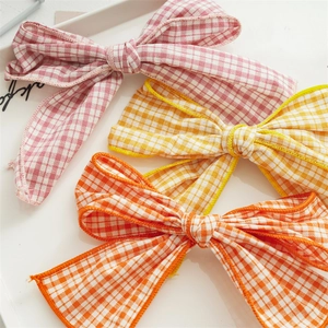 Close-up of pink, yellow, and orange checkered fabric bow hair clips on a white plate