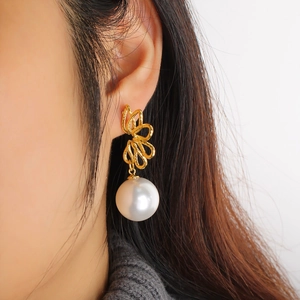 Detailed close-up of a large white pearl pendant on a gold hollow floral wreath earring