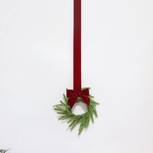 Artificial Norfolk pine wreath with a red velvet bow and hanging ribbon on white background