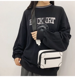 Close-up of white leather crossbody bag with black nylon strap worn by a model
