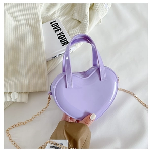 Detail of purple heart-shaped mini jelly bag with gold chain on white fabric