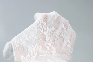 Close-up of white lace fabric with delicate floral patterns and mesh texture on a dress