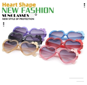 Flat lay of colorful heart-shaped kids' sunglasses with glitter frames and floral details