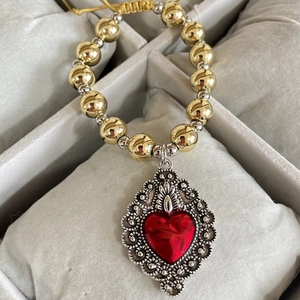 Detailed close-up of retro golden beaded bracelet with large red heart pendant and intricate carving