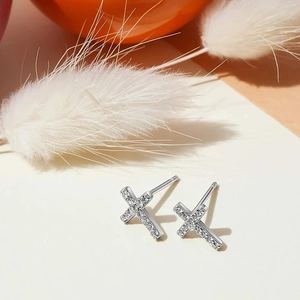 Close-up of cross-shaped silver earrings with sparkling zircon stones and a shiny finish