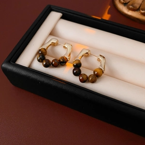 Macro shot of gold-plated U-shaped earrings with brown tiger eye beads on a display case