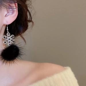 Detail shot of acrylic snowflake earring with soft black pom-pom on model ear