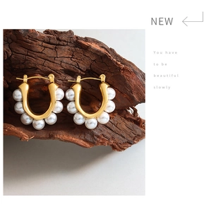 Detailed shot of French vintage U-shaped gold earrings with pearls on dark wood base