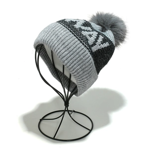 Detail view of a gray knit beanie with NORWAY jacquard pattern and faux fur pom-pom
