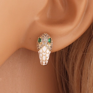 Close-up of gold snake earrings with white enamel scales and green gemstone eyes