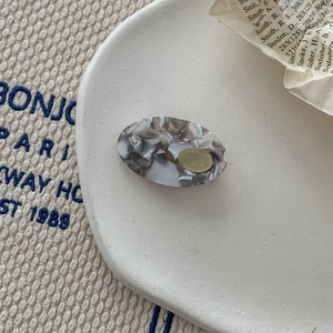 Close-up of oval acetate hair clip with grey-white marble texture on ceramic plate