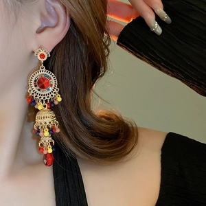 Close-up of vintage tassel earrings with gold base, red stone, and colorful beads