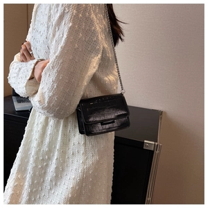 Model wearing a black crocodile embossed crossbody bag with a silver chain strap