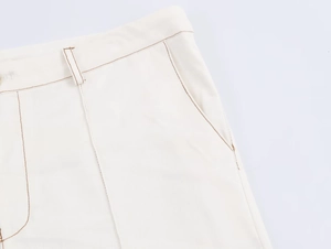 Detalle de pantalones acampanados blanco roto con costuras marrones y trabillas de cintura