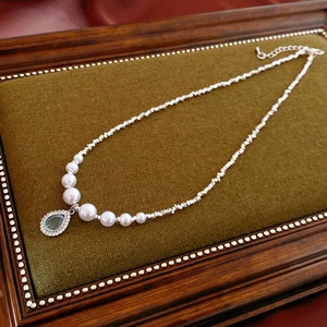 Detail of a pearl and silver bead necklace with a blue teardrop pendant on green velvet