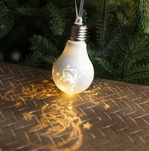 Christmas bulb ornament with warm LED light and starry projection on a pine branch