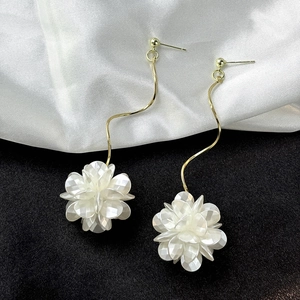 Detail of elegant gold wavy tassel earrings with 3D white shell flowers on silk fabric