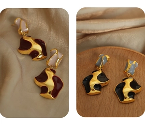 Detail of wavy asymmetrical gold-plated earrings with red and black enamel patterns