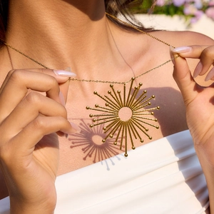 Golden 18K stainless steel sunburst pendant necklace shown with artistic shadow on skin