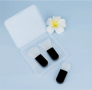 Three silicone face mask brushes with a clear storage box on a soft blue background