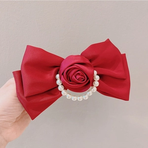 Detailed macro of a red velvet bow hair clip with faux pearl and rose center