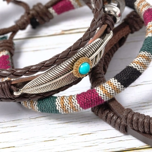 Detail of woven leather bracelet featuring a silver feather charm with turquoise stone inlay