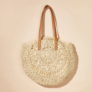 Detail of round straw bag showing intricate hollow-out weaving and brown leather straps