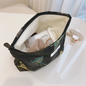 Detail of black jacquard makeup bag showing butterfly embroidery and interior lining