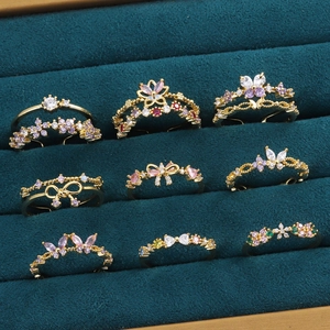 Détail de bagues papillon dorées serties de zircons colorés sur plateau vert