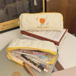 Quilted tulip pencil case with yellow zipper shown in a cozy study setting with pens