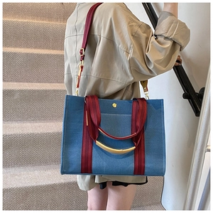 Detail of blue denim tote bag featuring red striped handles and metallic floral logo