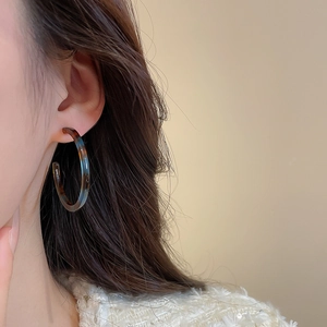 Detail of C-shaped tortoiseshell resin hoop earrings with amber and blue speckles on model