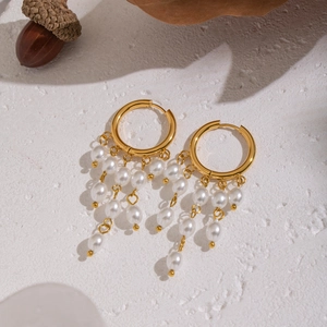 Close-up of gold hoop earrings with white pearl tassels on a textured white surface