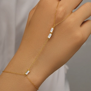 Close-up of golden finger chain bracelet with rectangular zircon accents on hands