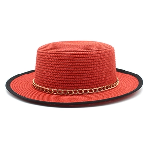 Détail d'un chapeau de paille rouge avec bord noir et chaîne dorée décorative