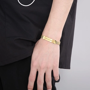 Close-up of a gold stainless steel mesh chain bracelet with a curved plate on a male wrist