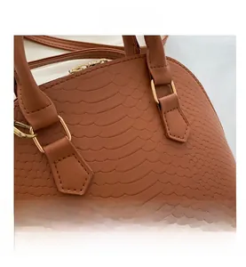 Detail of brown crocodile pattern handbag showing golden metal buckles and zipper hardware