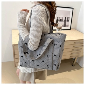 Model wearing grey corduroy tote bag with black bow and quilted diamond pattern