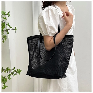 Detailed view of the large black mesh tote bag worn on a shoulder against a white wall