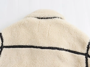 Close-up of beige shearling jacket with black faux leather trim on the collar and seams