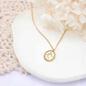 Detail of gold sunburst star pendant on a ceramic tray with white dried flowers