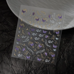 Macro detail of 3D embossed nail stickers with purple butterflies and gold flowers