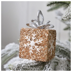 Detailed glittery golden Christmas gift box ornament with a white snowflake on a snowy branch