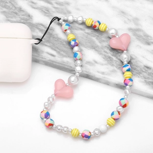 Bijou de téléphone perlé avec fausses perles et cœurs roses sur fond de marbre blanc