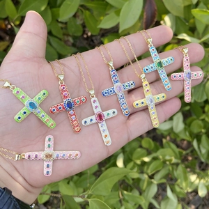 Close-up of hand holding various colorful enamel cross pendants with zircon inlays