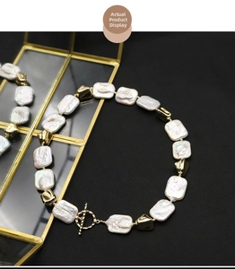 Macro detail of baroque pearl necklace featuring golden OT clasp on textured background
